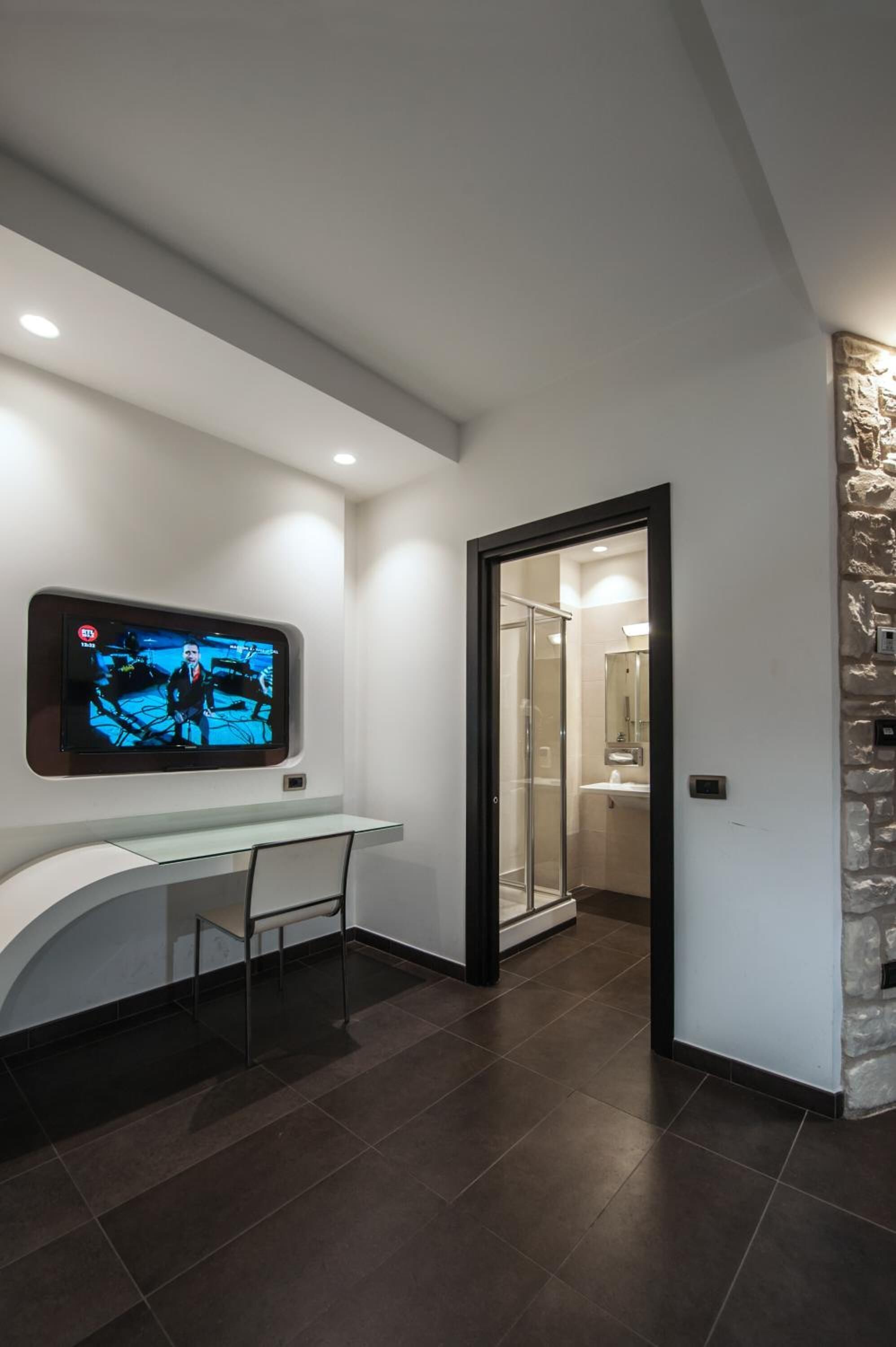 Un baño moderno con cabina de ducha de vidrio, televisor montado y tocador blanco.