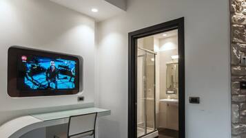 Un baño moderno con cabina de ducha de vidrio, televisor montado y tocador blanco.