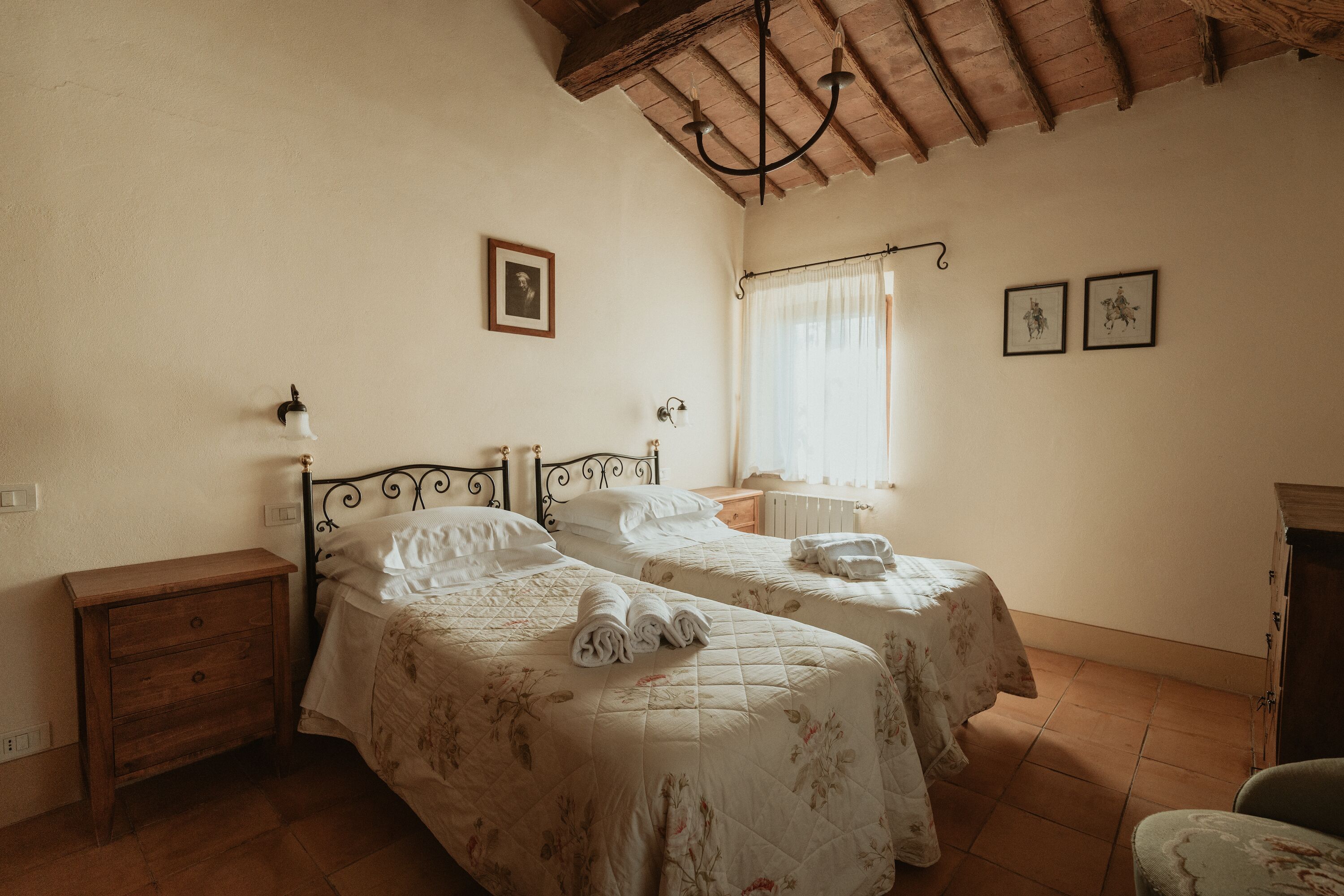 Un dormitorio con dos camas, una mesita de noche de madera, una lámpara de pared y una ventana con cortinas.
