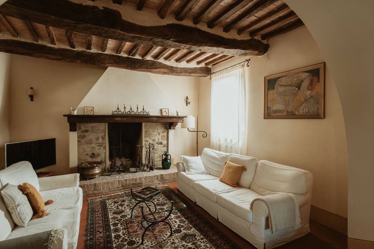 A cozy living room with a fireplace, white sofas, and a patterned rug.