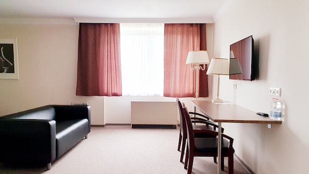 A hotel room with a black sofa, a wooden dining table with chairs, a lamp, a TV, and a radiator. - Hotel Pause (Hofheim am Taunus)