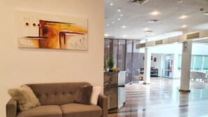 A modern lobby with a grey sofa, a marble reception desk, and a large abstract painting. - Hotel Pause (Hofheim am Taunus)