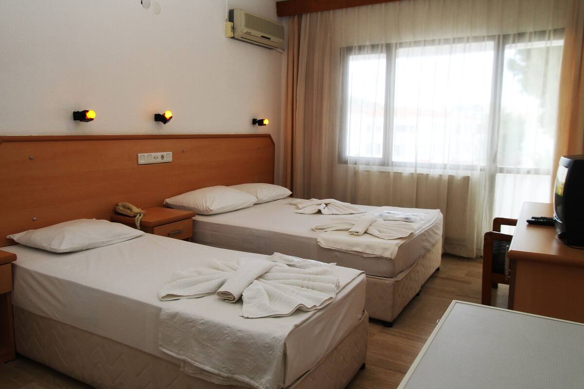 A hotel room with two beds, a bedside telephone, a desk with a television, and a window with curtains.