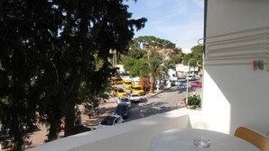 A balcony with a table and chairs, overlooking a street with parked cars and a building in the background.