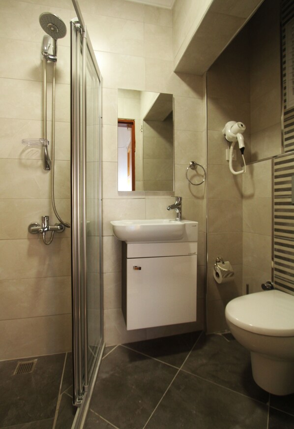 A bathroom with a glass shower enclosure, a sink, a toilet, and a mirror. - Goren Hotel (Cesme)