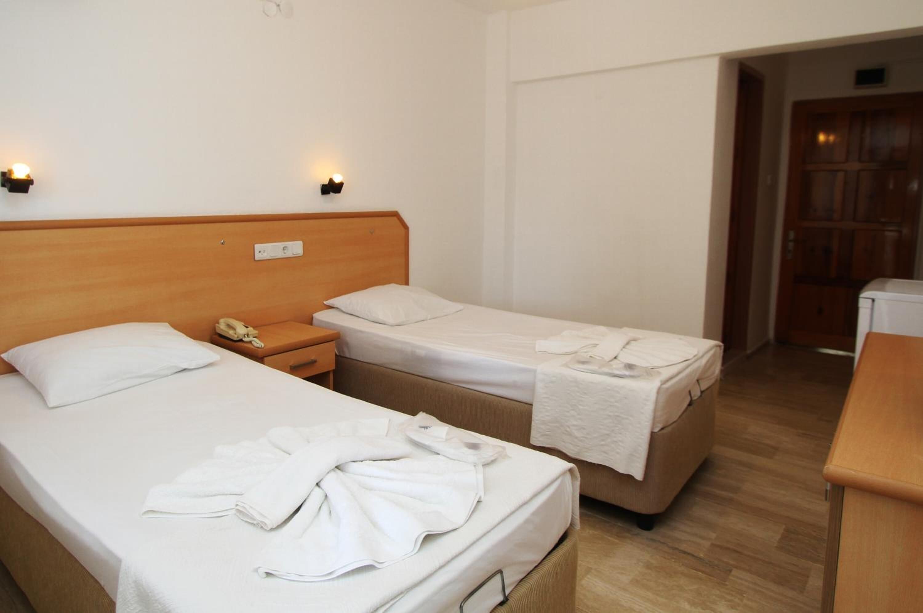 A hotel room with two single beds, a wooden headboard, bedside tables with lamps, and a wooden desk.
