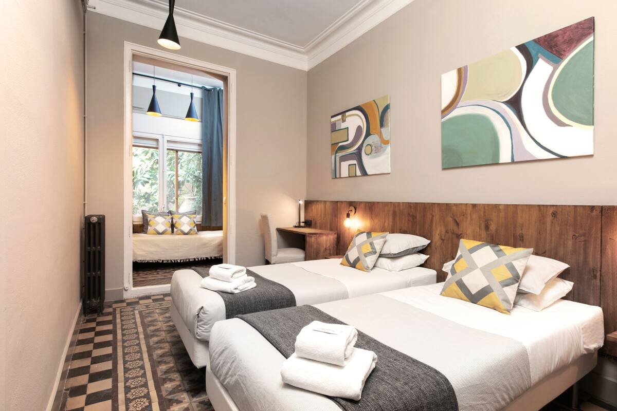 A hotel room with two beds, a checkered floor, abstract wall art, and a window with curtains.