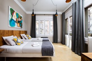 A hotel room with two beds, a large abstract painting, and a view of buildings through the window. - Jardinets Guest House (Barcelona)
