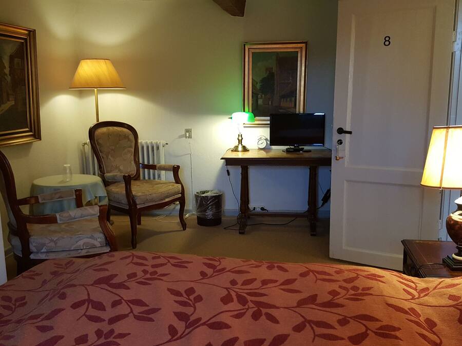 Habitación de hotel con cama, escritorio con computadora, silla, lámpara y un cuadro en la pared.