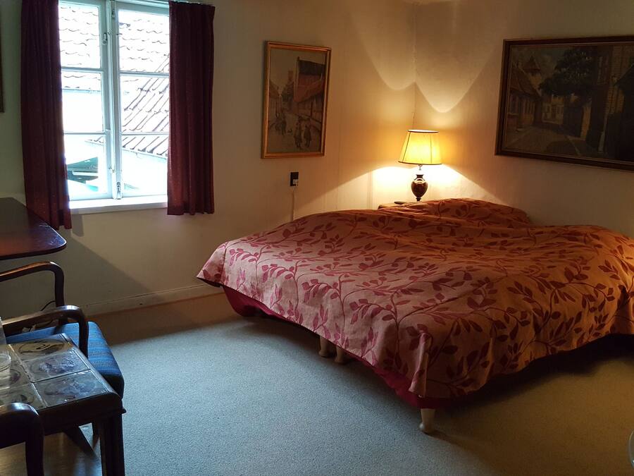 Un dormitorio con cama, un escritorio con lámpara, una silla y una ventana con cortinas.