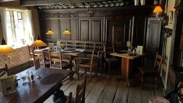 A rustic dining area with wooden tables and chairs, pendant lights, and a vintage decor.