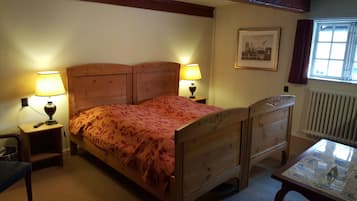 A wooden bed with a floral bedspread, two bedside lamps, a framed picture on the wall, a window with curtains, and a small table with a glass.