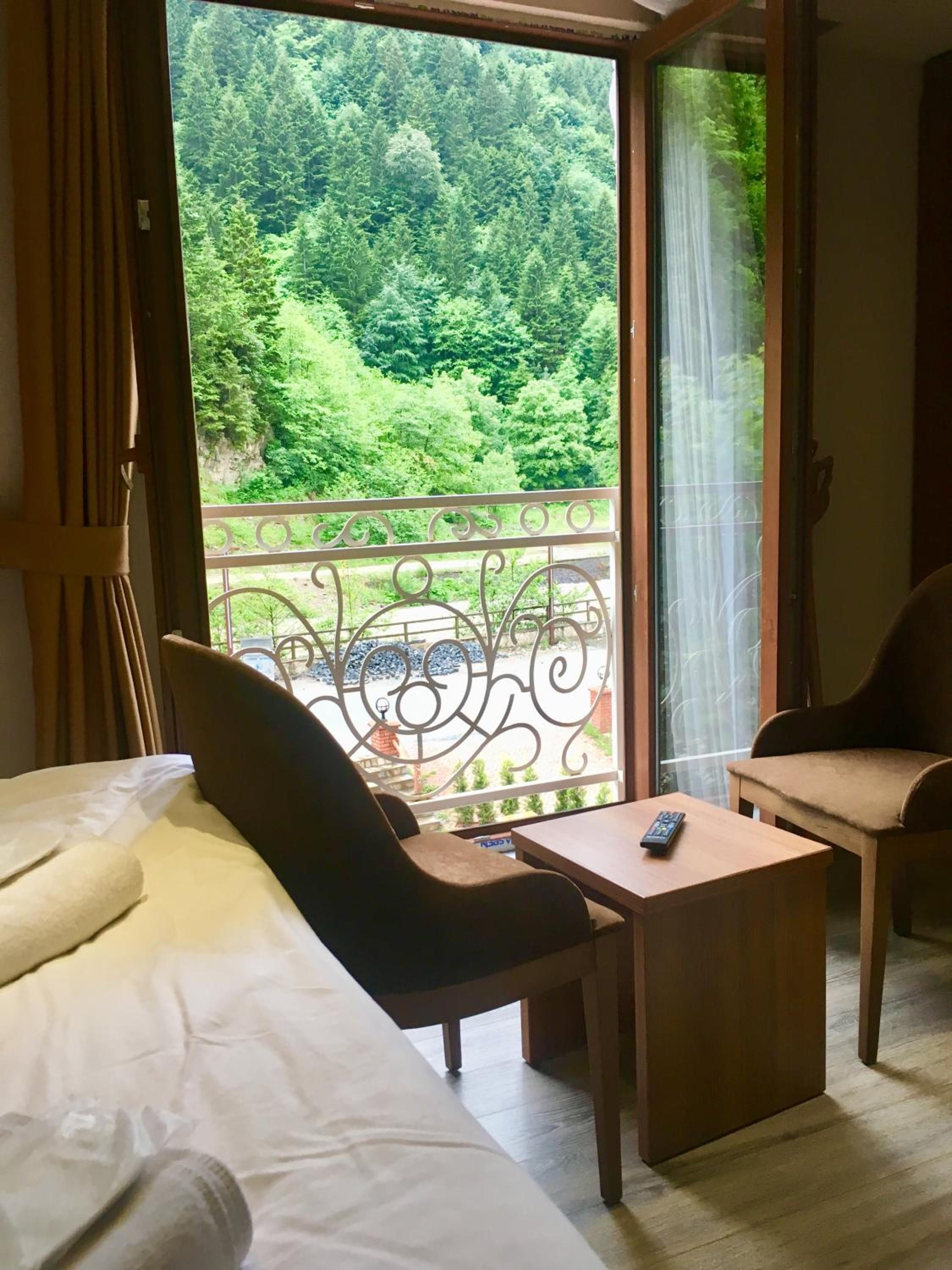 A room with a bed, a desk, and a chair, with a balcony overlooking a forest.
