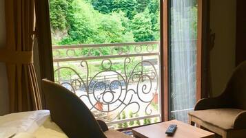 A room with a bed, a desk, and a chair, with a balcony overlooking a forest.