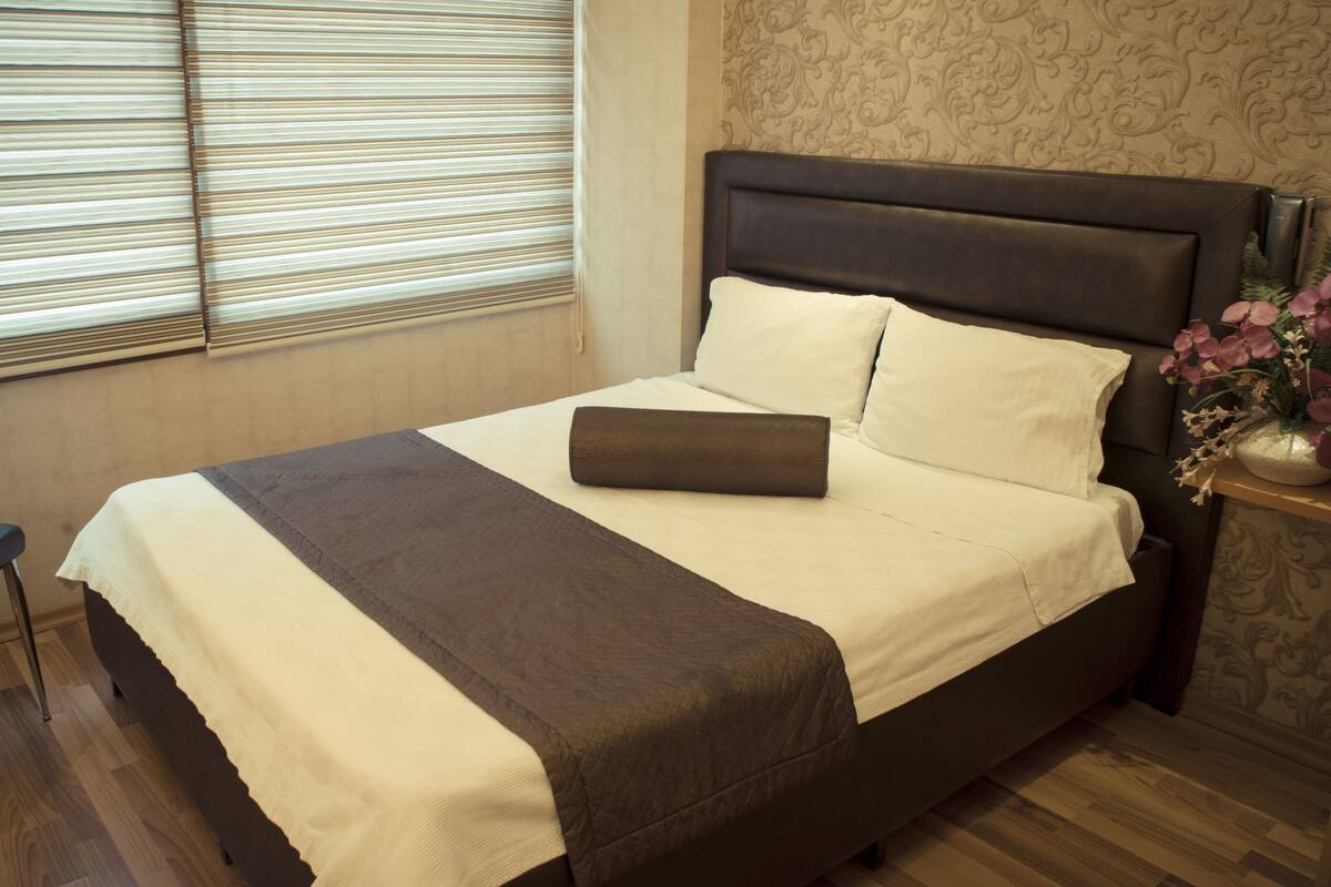 A neatly made bed with a dark headboard, a bedside table with a vase of flowers, and a chair.