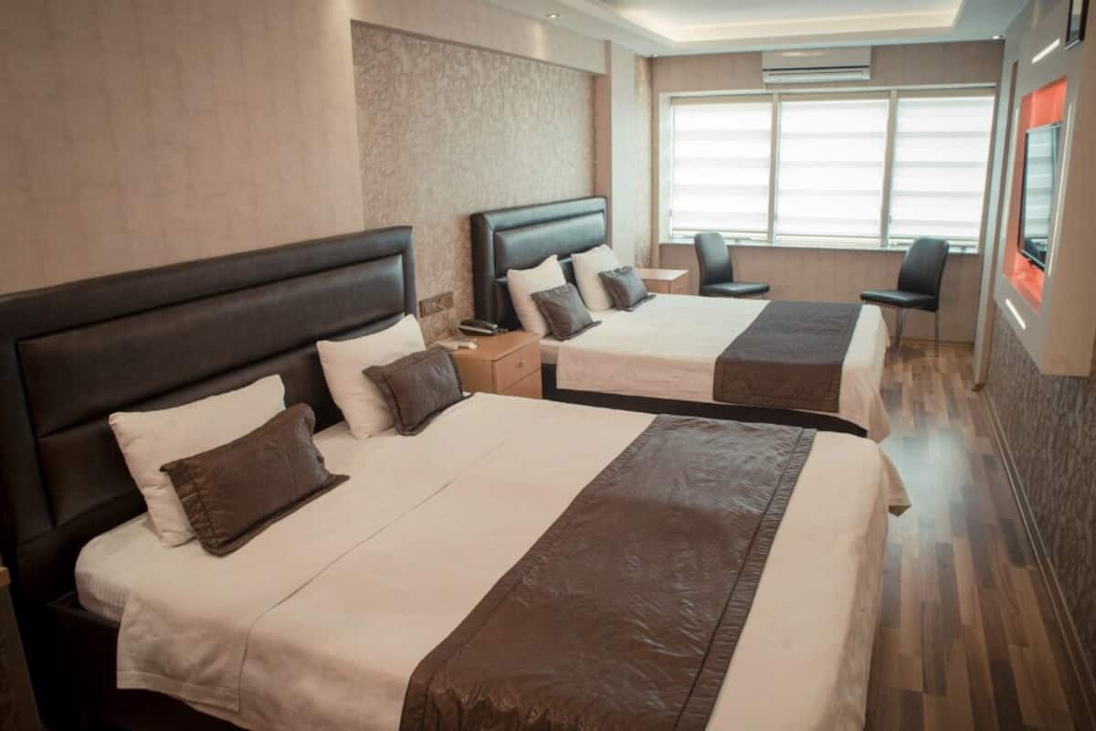 A hotel room with two beds, each with a headboard, a bedside table, and a chair.
