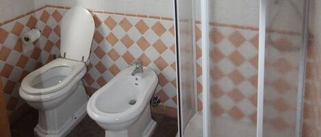 A bathroom with two toilets, a bidet, and a shower.