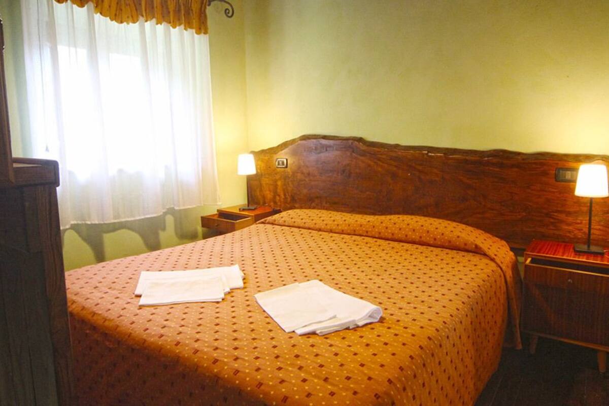 Een hotelkamer met een houten hoofdeinde, twee bedlampjes, een bed met een geborduurde spreideken en twee opgevouwen handdoeken op het bed.
