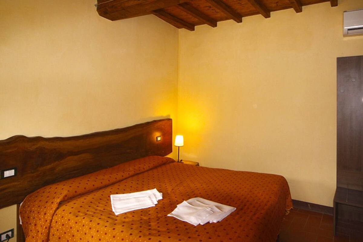 Een hotelkamer met een houten hoofdeinde, een bed met een geborduurde spreideken, een bedlamp en een ingebouwde televisie.