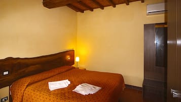 A hotel room with a wooden headboard, a bed with a patterned bedspread, a bedside lamp, and a built-in TV.
