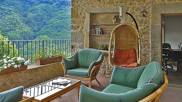 Un balcon agrémenté de meubles en osier, d’une table en verre et offrant une vue sur un paysage montagneux.