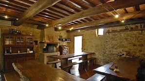 Une pièce rustique aux murs de pierre, avec des poutres apparentes, une grande table en bois et une cheminée.