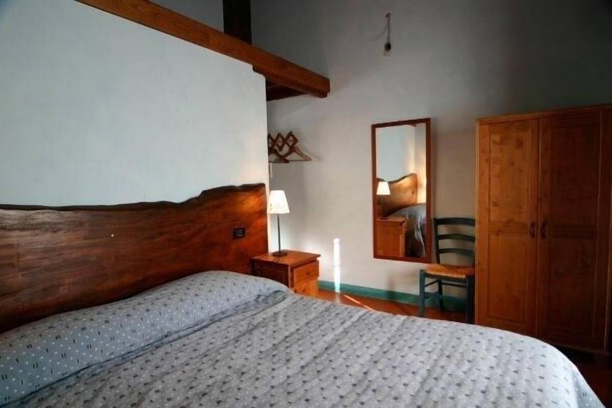 Een slaapkamer met een houten hoofdbord, een bed met een bedovertrek met een patroon, een nachtkastje met een lamp, een houten garderobe en een spiegel aan de muur.
