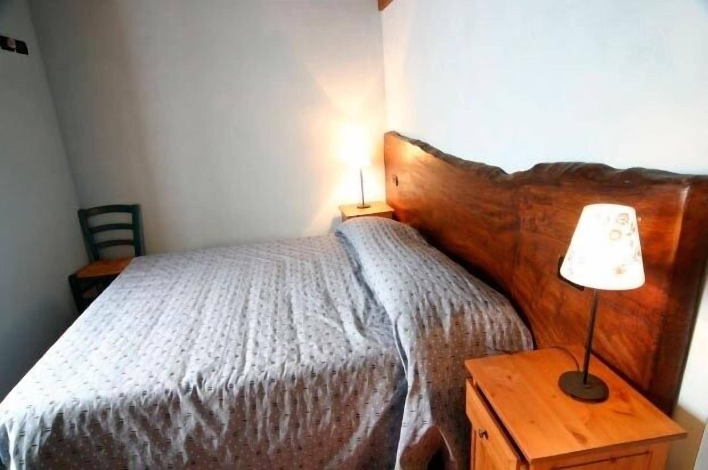 Een klein, net opgemaakt bed met een houten hoofdbord en een nachtkastje met een lamp.
