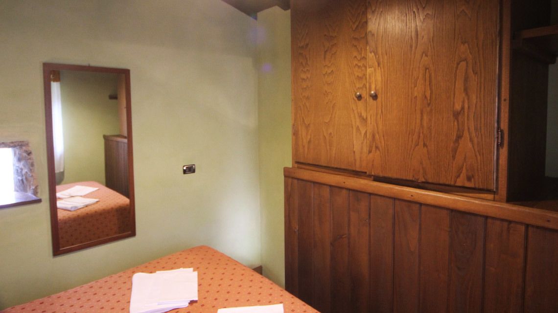 Una stanza con un letto, un armadio in legno e uno specchio a parete.