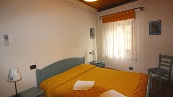 A bedroom with a bed, a nightstand, a chair, a window with curtains, and a wall-mounted lamp.