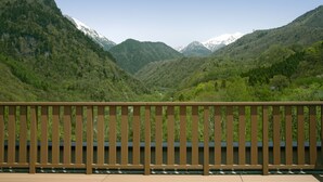 Holzgeländer eines Balkons mit Blick auf ein Tal, Berge und einen klaren Himmel.