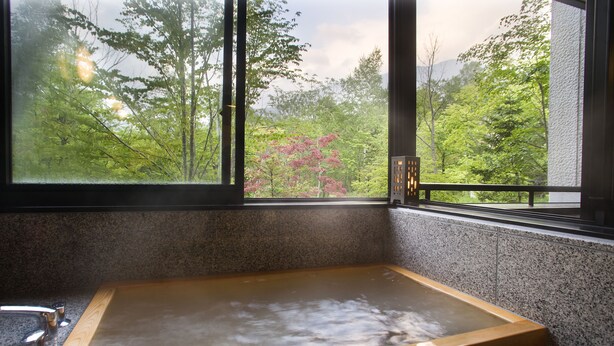 Ein hölzernes Quellbad mit Blick auf einen Wald durch ein Fenster.