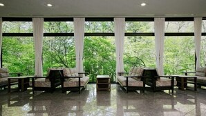 Ein geräumiger Raum mit großem Fenster, zwei Sofas, einem kleinen Tisch und Fliesenboden.