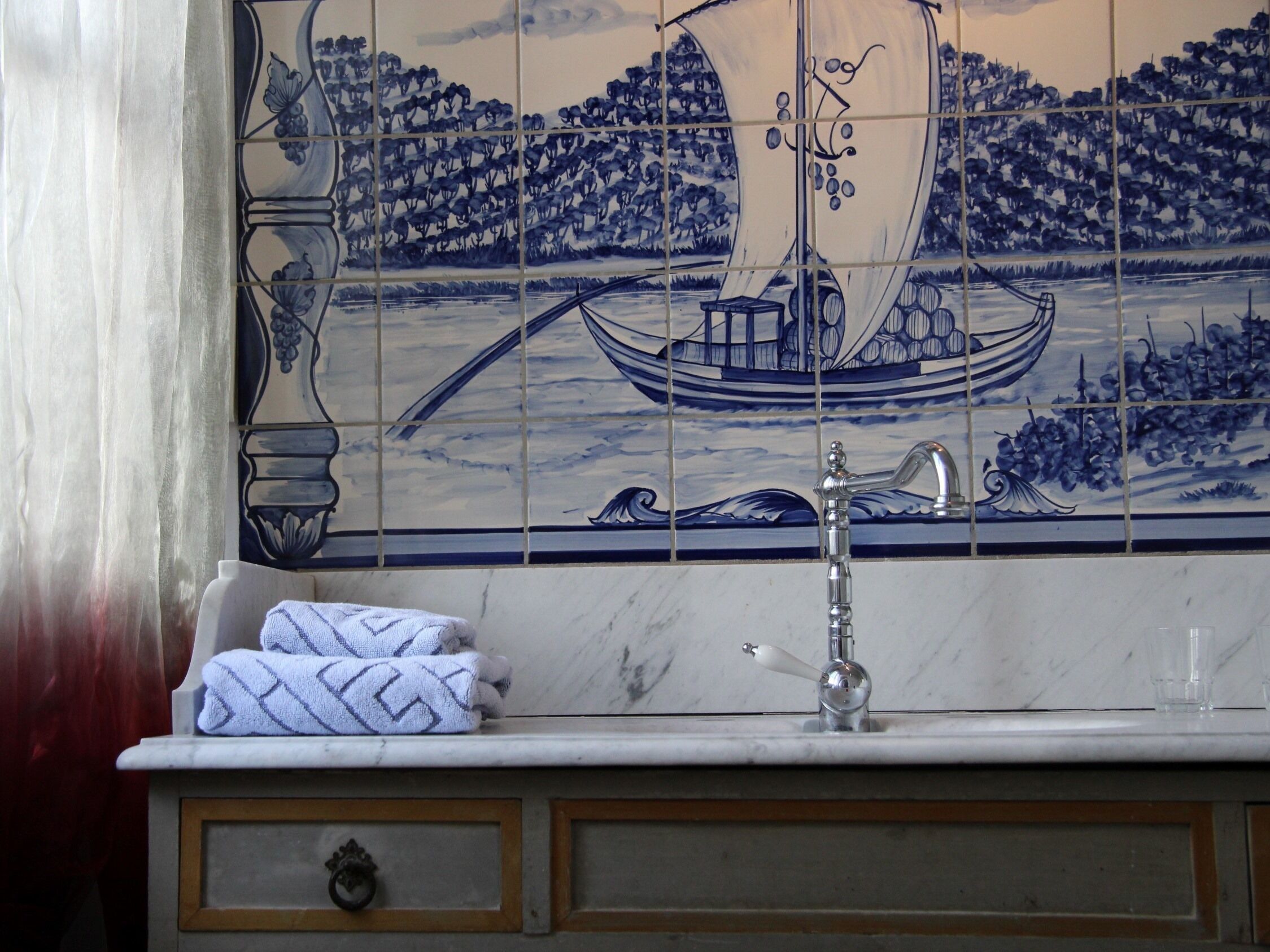 Ein Badezimmer mit Fliesen an der Wand, die ein Segelschiff zeigen, einem Waschbecken und einem Handtuch.