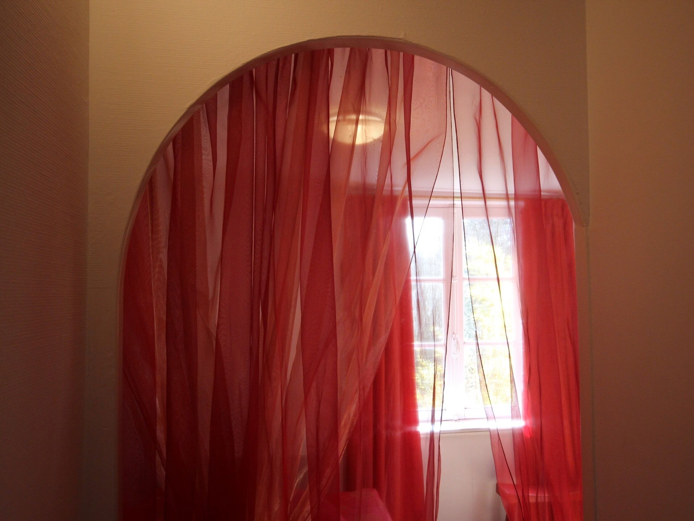 A room with a large arched window covered by sheer red curtains.