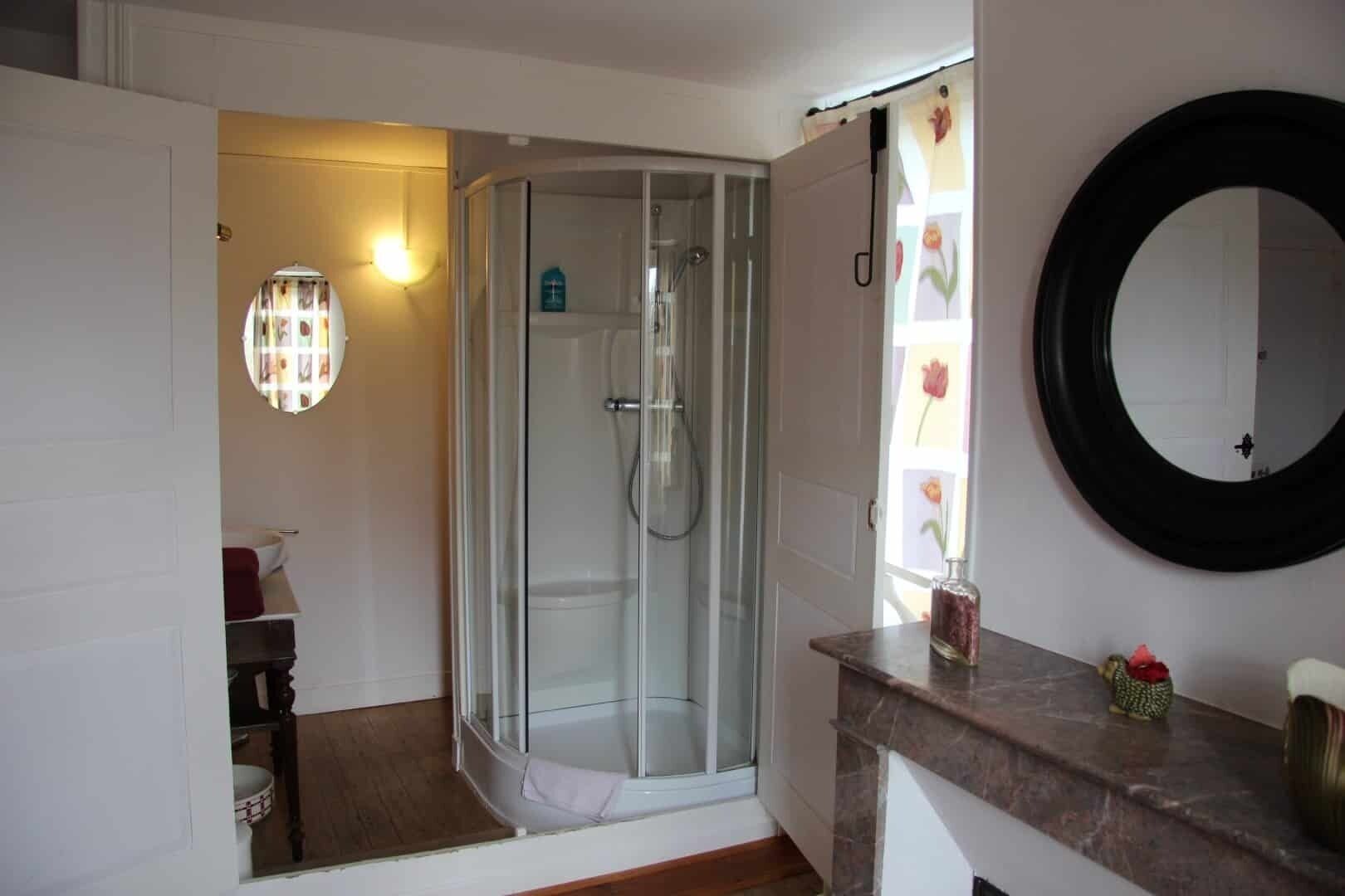 A bathroom with a glass shower enclosure, a round mirror, and a marble countertop.