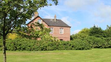 A brick house with a chimney, surrounded by lush greenery and a well-maintained lawn.