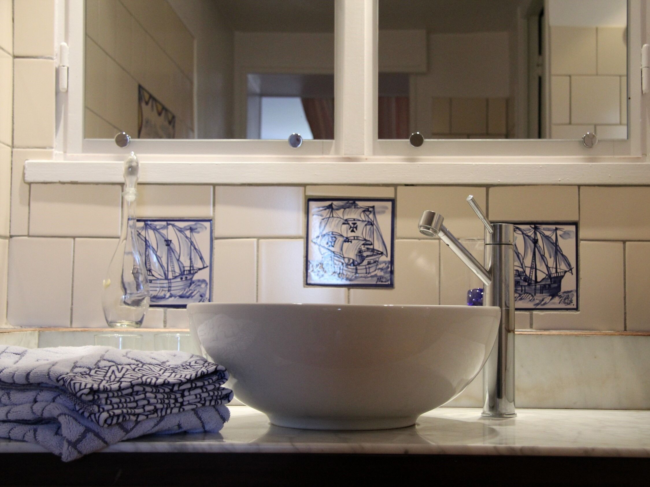A bathroom with a large white basin, a mirror, and tiled walls with nautical-themed artwork.