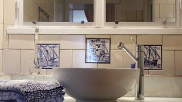A bathroom with a large white basin, a mirror, and tiled walls with nautical-themed artwork.