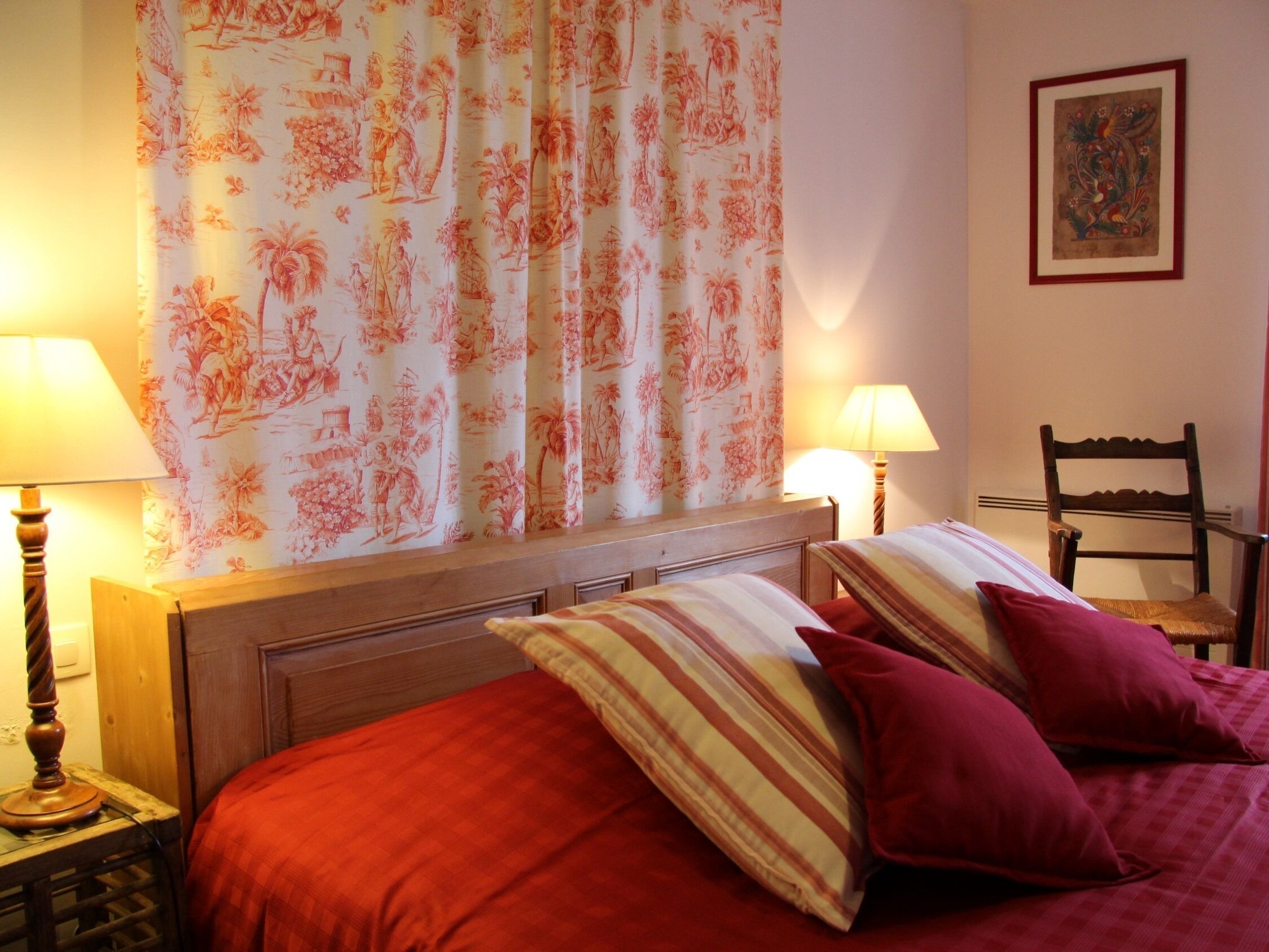 A bedroom with a bed, two bedside lamps, a chair, and a painting on the wall.