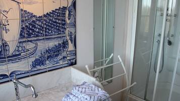 A bathroom with a tiled wall, a sink, a mirror, a towel rack, and a shower enclosure.