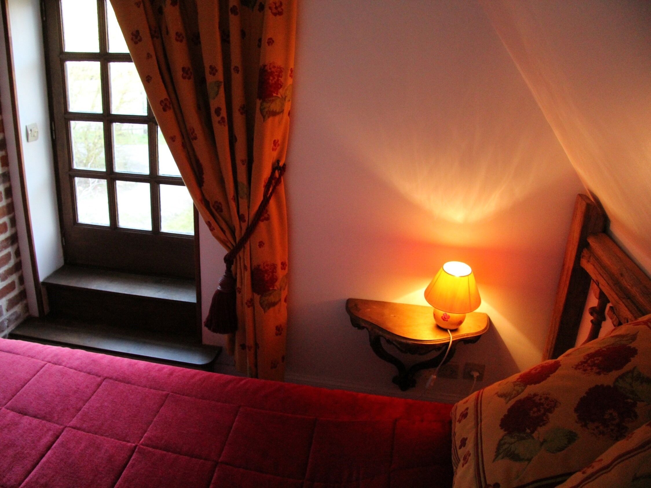 A room with a bed, a window with curtains, a lamp, and a wooden bench.