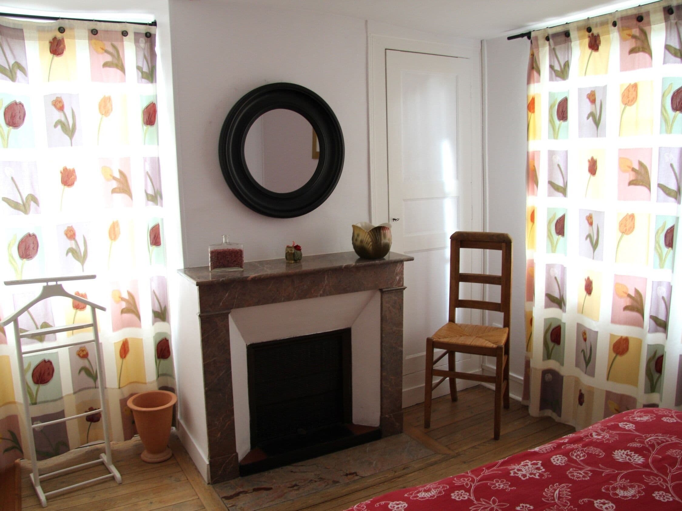 A room with a fireplace, a mirror, a chair, a small table, and a hanging rack.