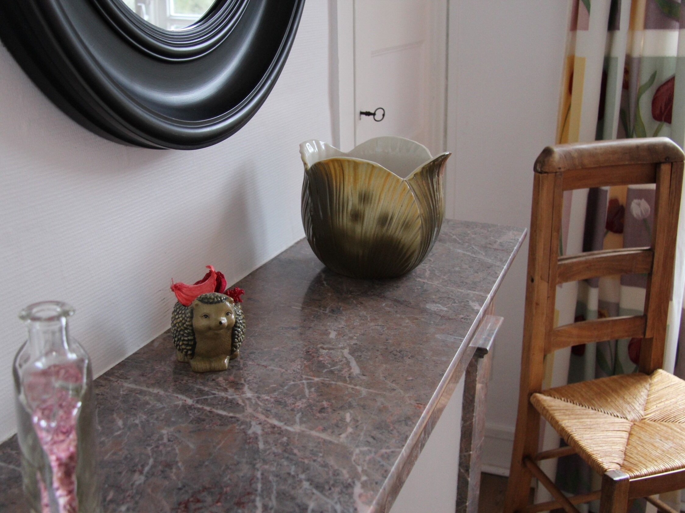 Un plan de travail en marbre agrémenté d’un bol décoratif, d’une petite figurine et d’une bouteille en verre.