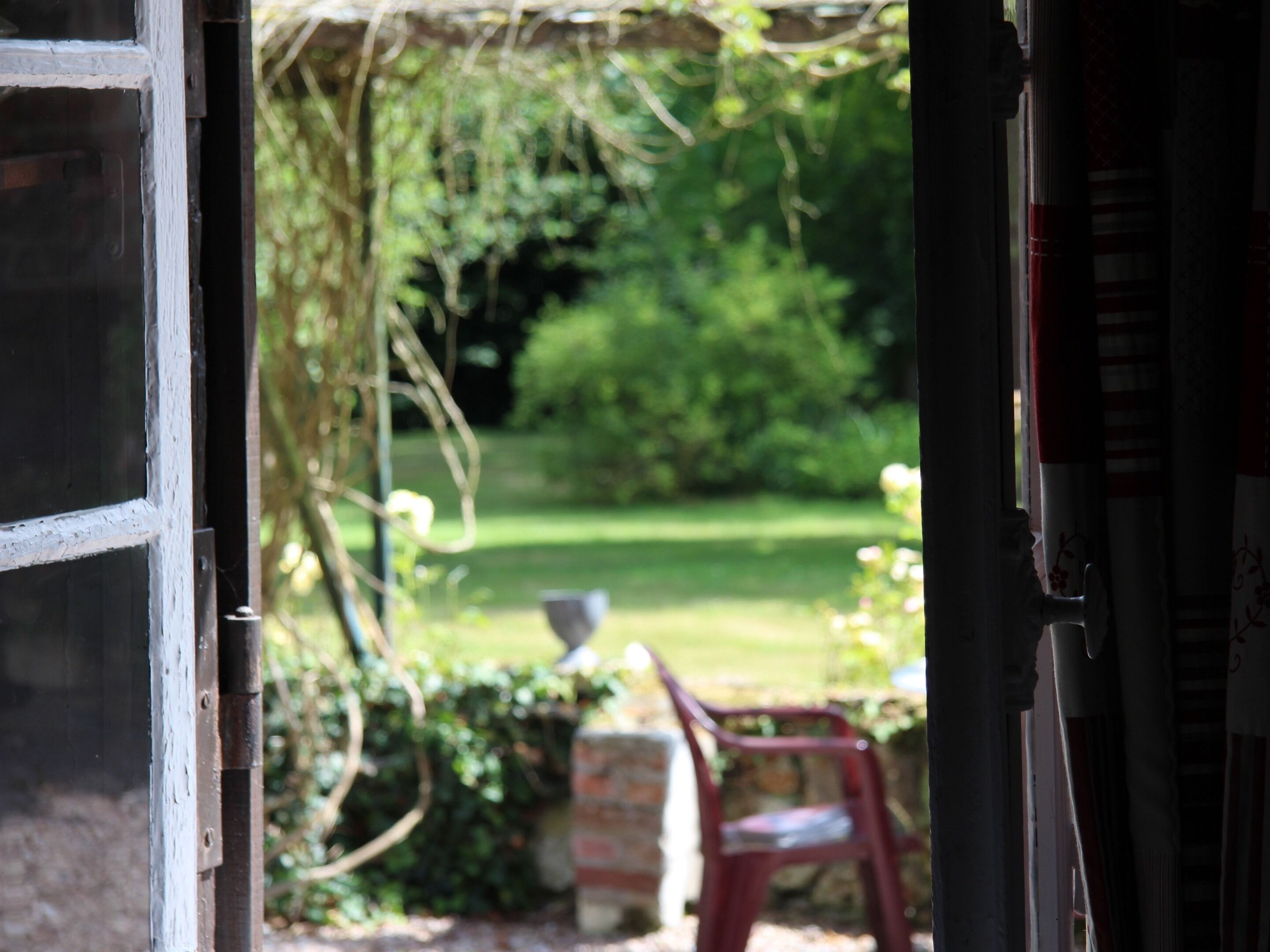 An open door leading to a garden with a lawn, a red chair, and a stone structure.