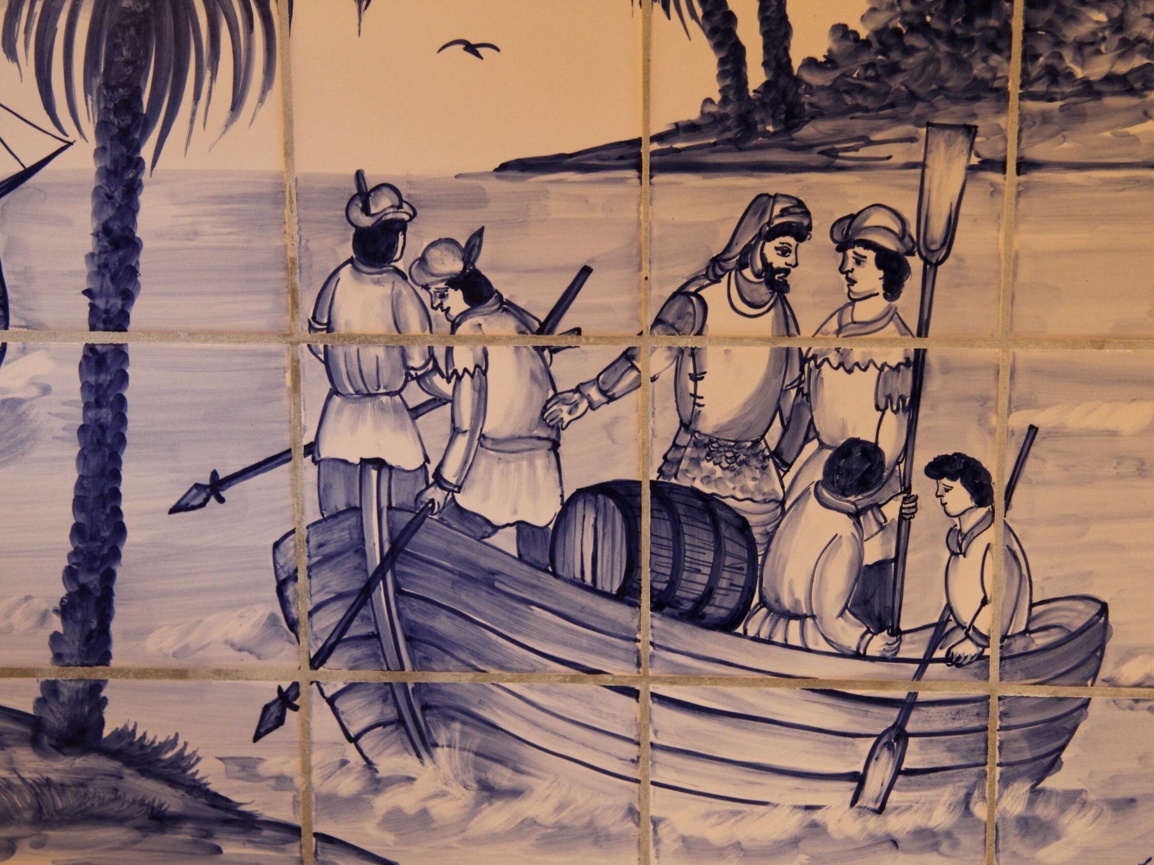 A tiled wall with a maritime scene depicting people in a boat, palm trees, and a bird in the sky.