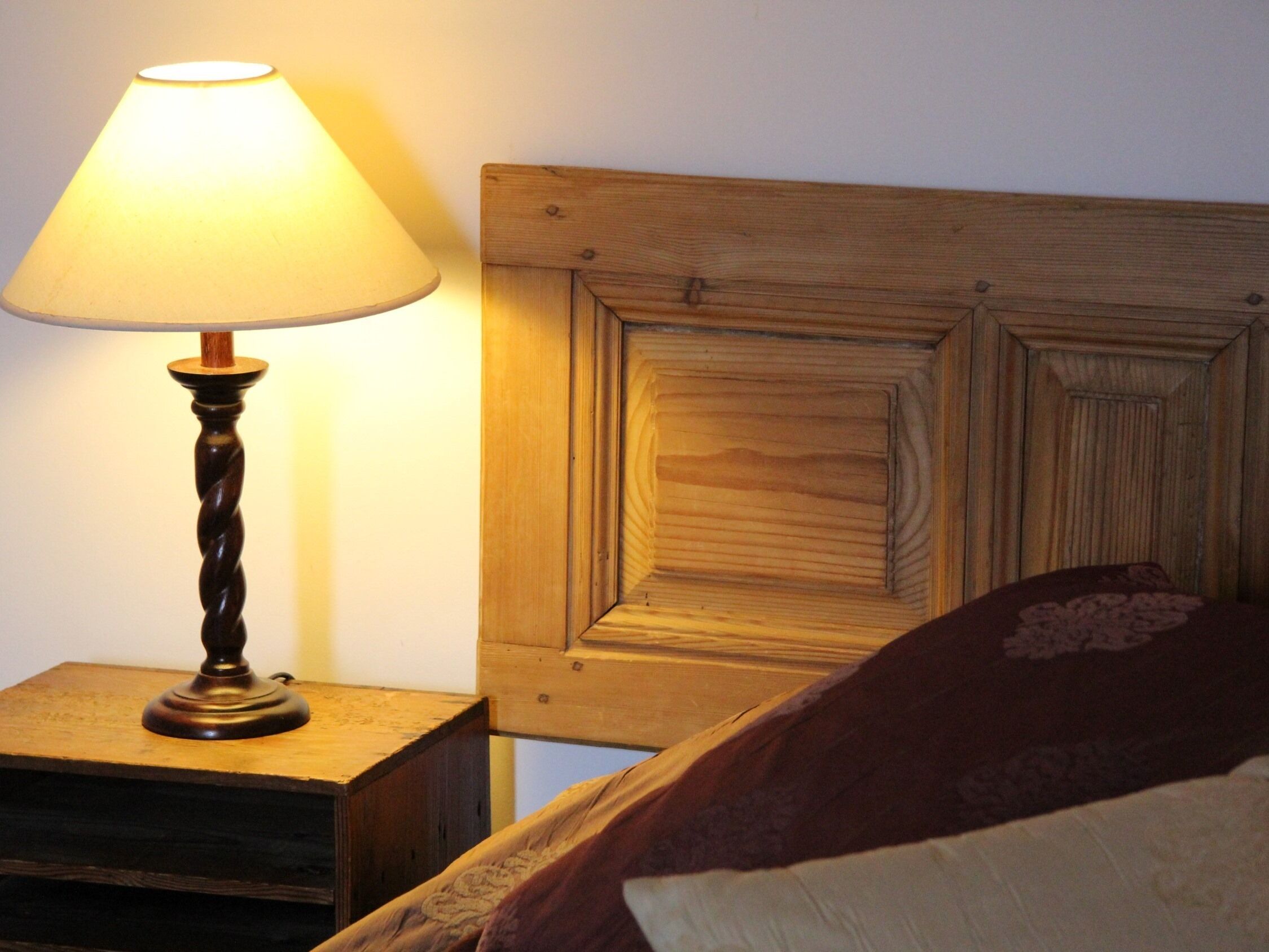 Cabecera de madera con diseño sencillo, mesita de noche con lámpara y cama con almohada estampada.