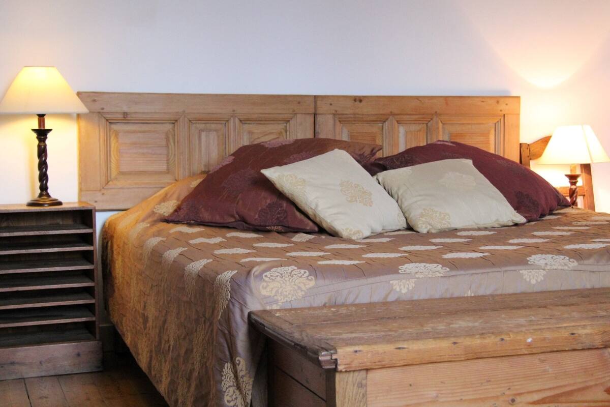 Una cama de madera con cabecera, dos lámparas de noche y una colcha estampada.