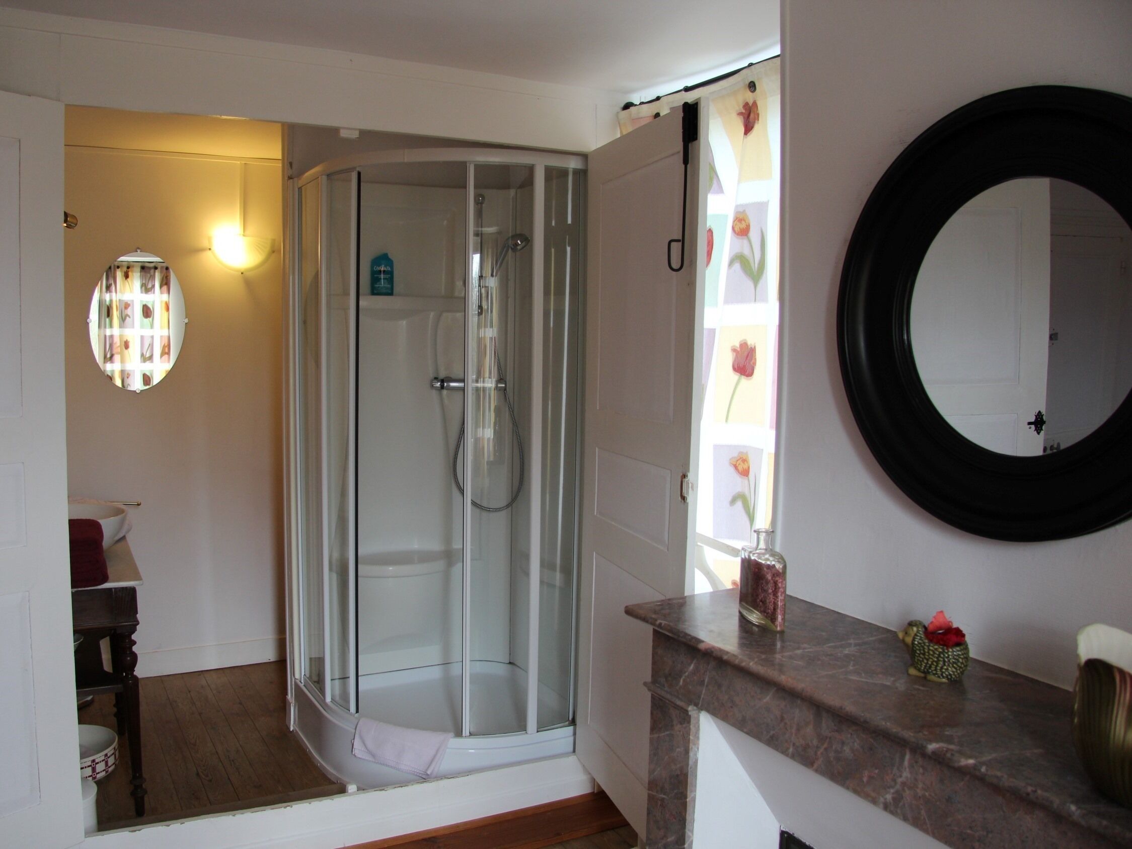 Een badkamer met een douchecabine van glas, een ronde spiegel en een marmeren aanrechtblad.
