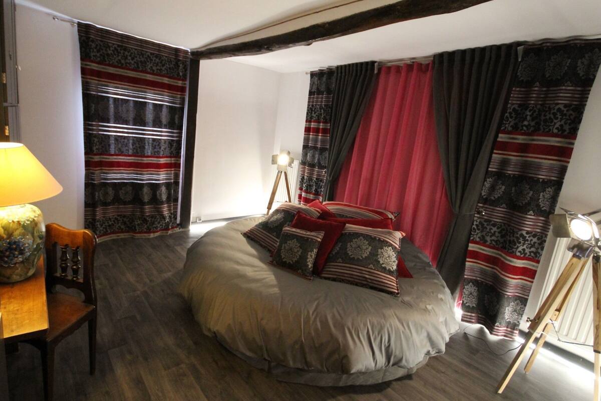 Un dormitorio con cama redonda, un escritorio con lámpara, una silla y una lámpara trípode.